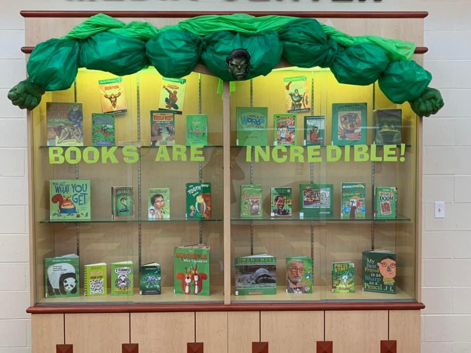 A display case with books inside of it has words across the front that says Books are Incredible. There is green tissue paper and a face across it that is meant to look like the Incredible Hulk.