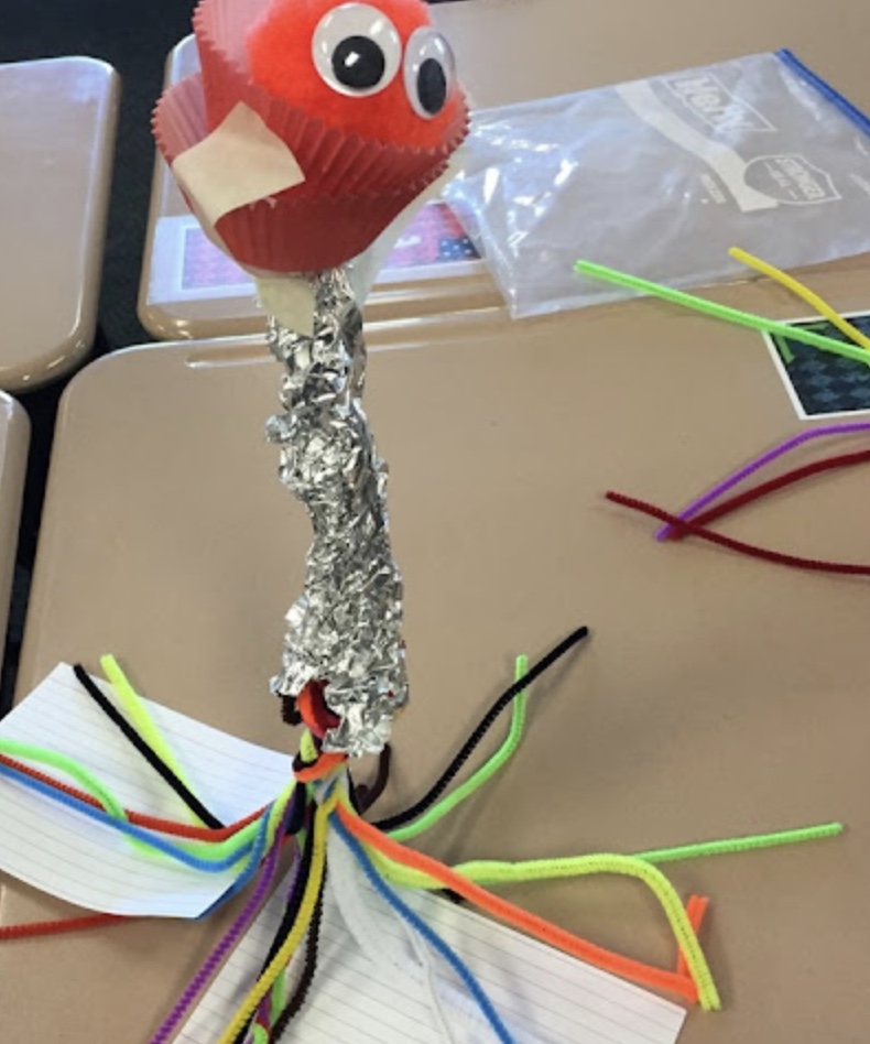 pom pom sitting on a perch made of tin foil and pipe cleaners 