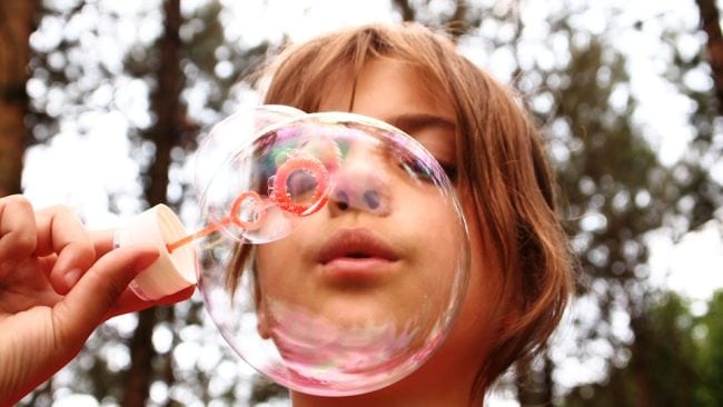 Child using a plastic wand to blow soap bubbles