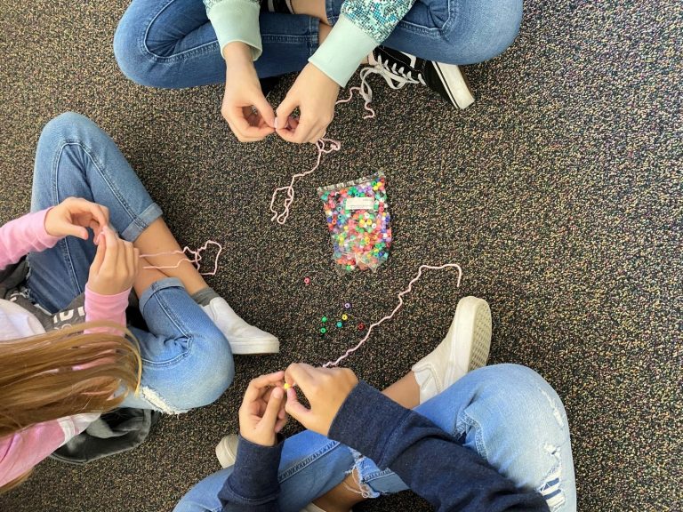 Aerial view of kids sitting cross-legged on a rug making bead necklaces pi day activities