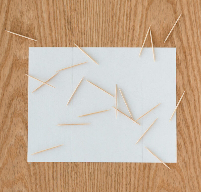 A piece of white paper on a wood surface with wood toothpicks scattered across it