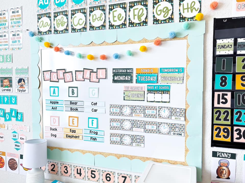 A Board says Word Wall and has a few words on it for students to learn. There are other items on the board like clocks showing what time each subject would be taught.