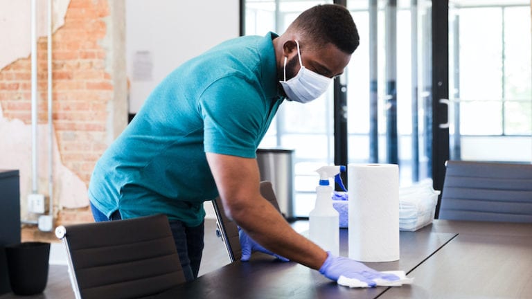 Man cleans table in office during COVID-19