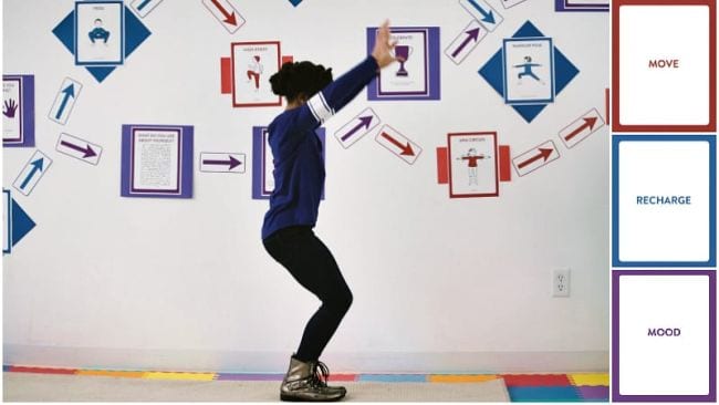 Child doing a yoga pose in front of a school wall with various movement posters
