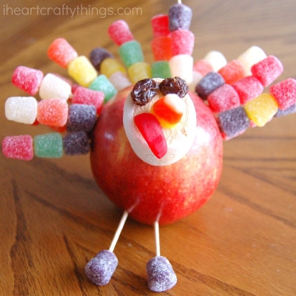 An apple made to look like a turkey with juju fruit feathers and a marshmallow head