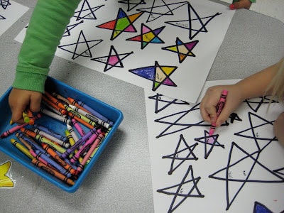 Child drawing five pointed stars and coloring them in with crayons