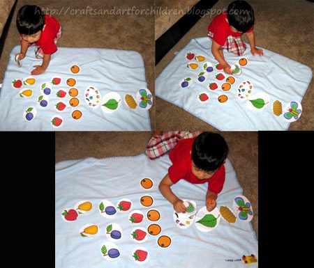A young child is seen on a white blanket with different fruit printables spread out.