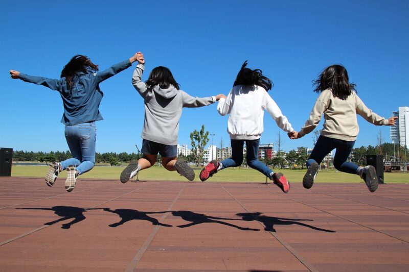 Four children holding hands and jumping, as an example of types of play