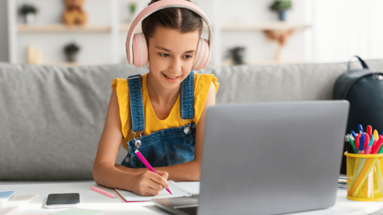 Girls wearing headphones, watching drawing videos for kids on a laptop and drawing with a marker on a piece of paper.