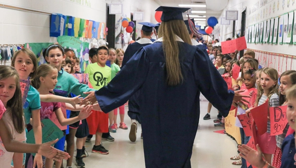 hHgh school graduates walking through the halls of their elementary school giving students high fives