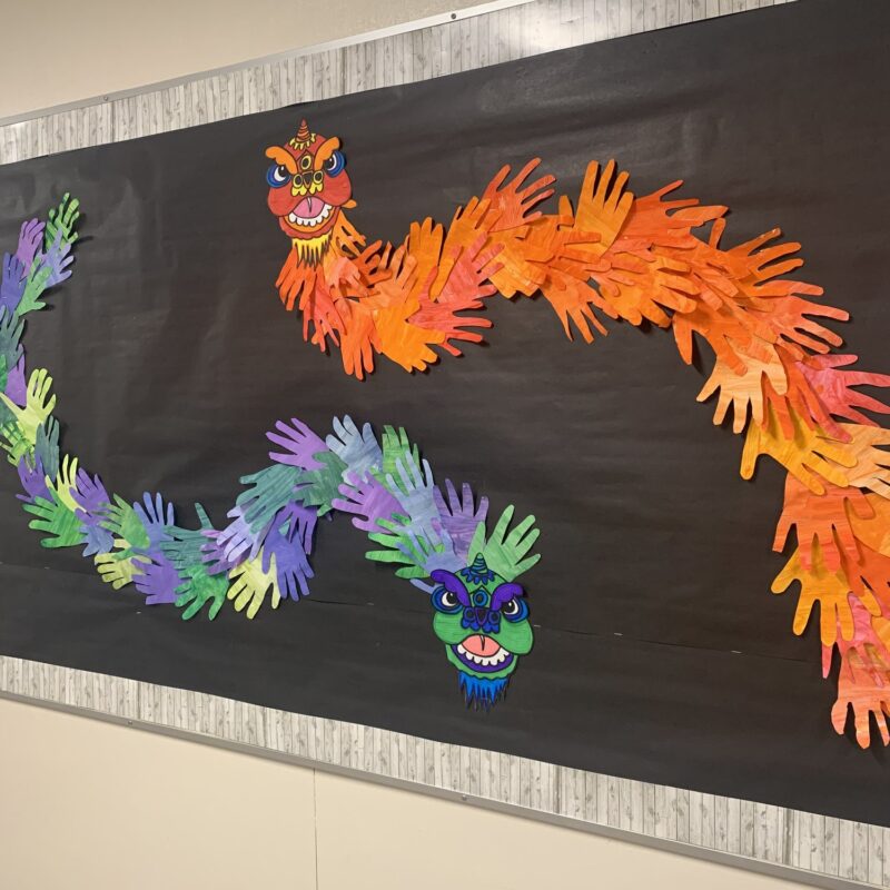 Colorful paper dragons made from painted handprints on a black bulletin board