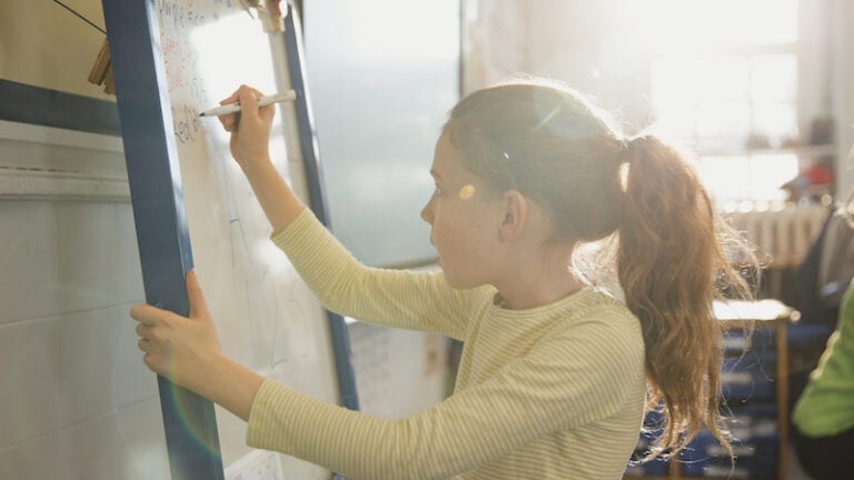 An elementary schoolgirl wearing casual clothing writes on a whiteboard in class -- interactive writing.