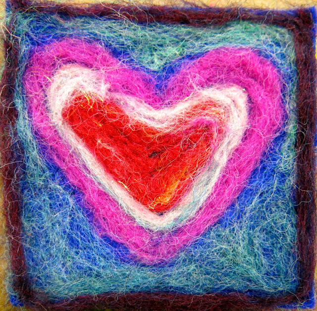 Needle felted heart in pink, white, and red against a blue-green background