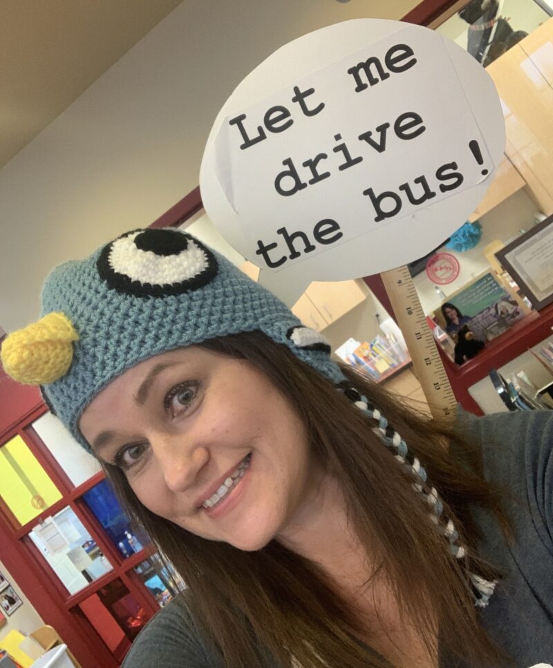 Teacher dressed as Mo Willem's pigeon, with a sign saying Let me drive the bus!