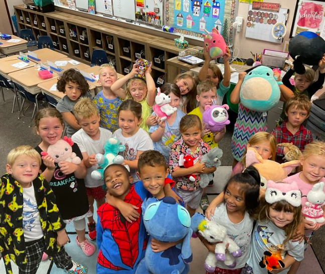 Smiling children wearing pajamas and holding stuffed animals in the classroom