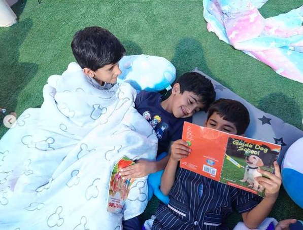 Three boys snuggled up under blankets reading a book together as an example of pajama day ideas and activitie