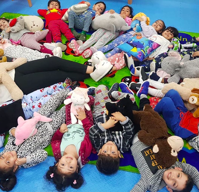 School children wearing pajamas laying in a circle with all of their feet in the middle 