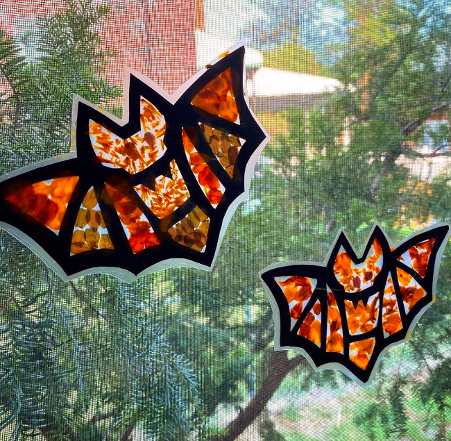 A black-outlined bat shape is filled in with splotchy orange paint as an example of halloween crafts for kids