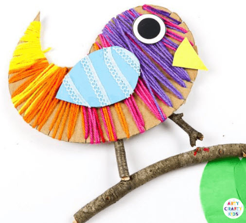 Simple cardboard bird shape wrapped in colorful yarn and sitting on a twig